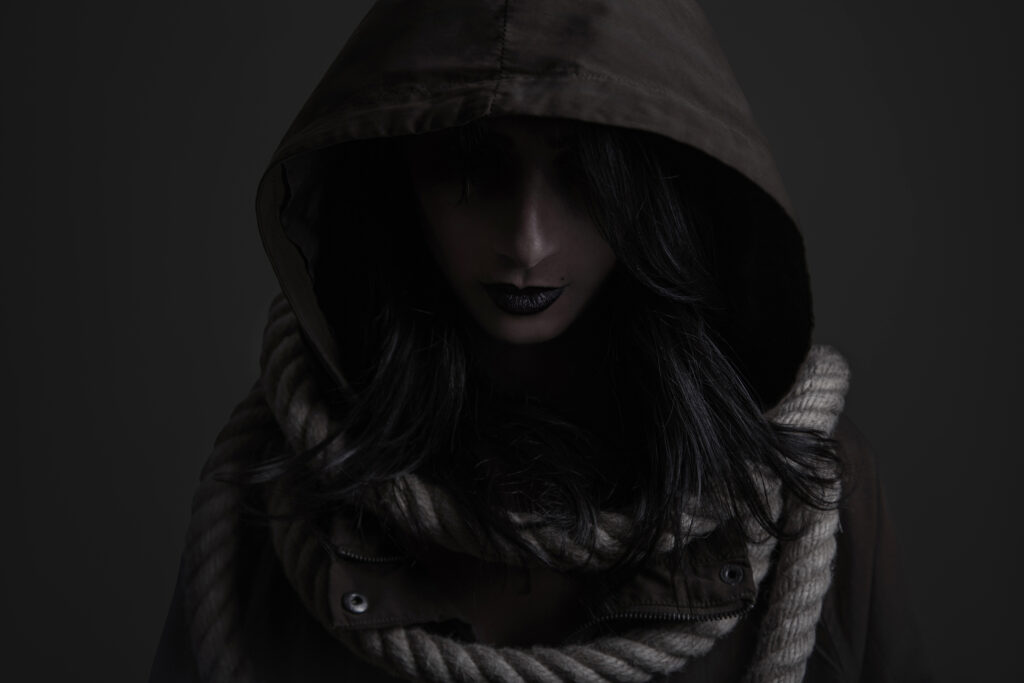 Portrait éditorial en studio d’une femme en capuche, ambiance sombre inspirée d’un univers occulte, série Coven créée par Armando Garcia