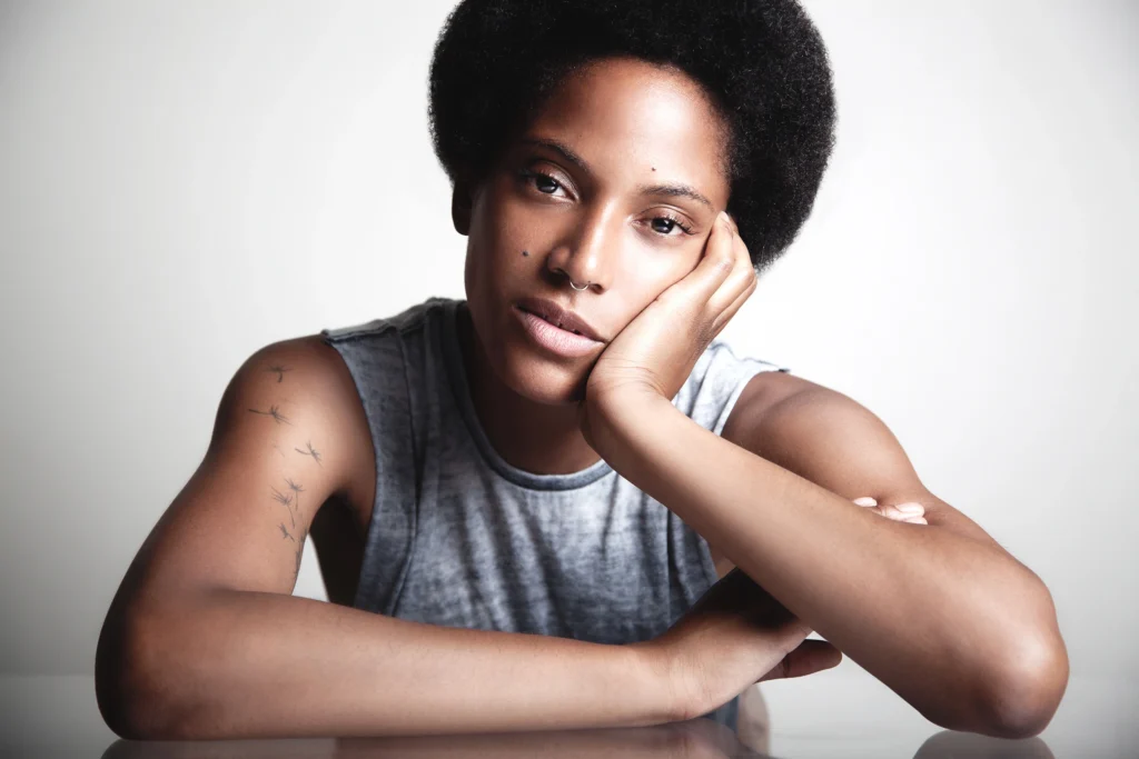 Portrait éditorial en studio d’une femme accoudée à une table en verre, ambiance claire et posée, photographie réalisée par Armando Garcia